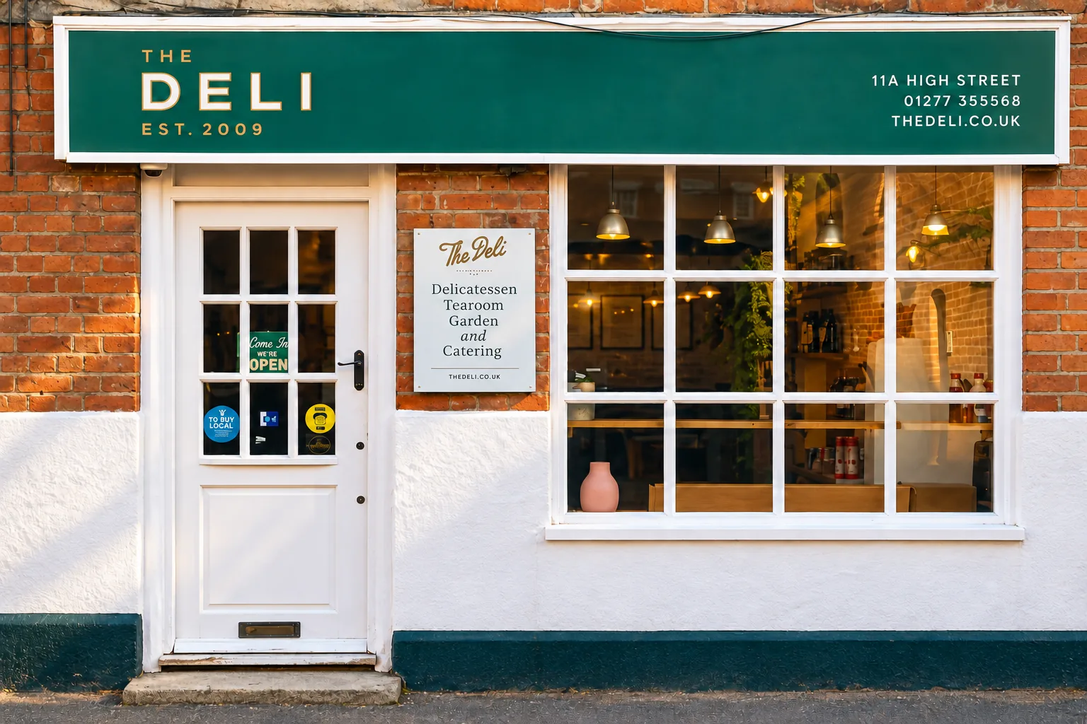 AI illustration based on published reference imagery for The Deli, Ingatestone: green deli fascia, white door and grid window at 11a High Street. Not an actual photograph.